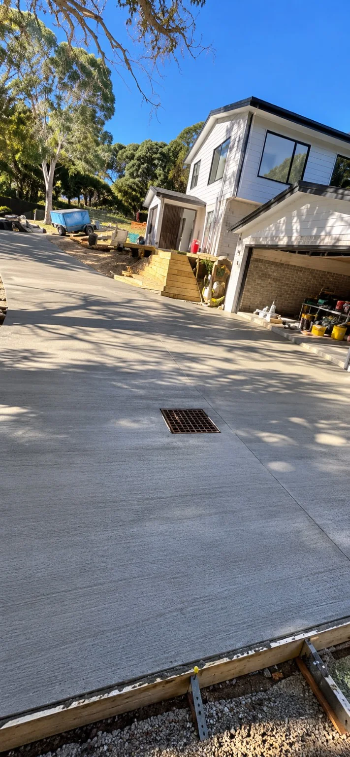 Large poured driveway with drainage inlet near a new two-storey home